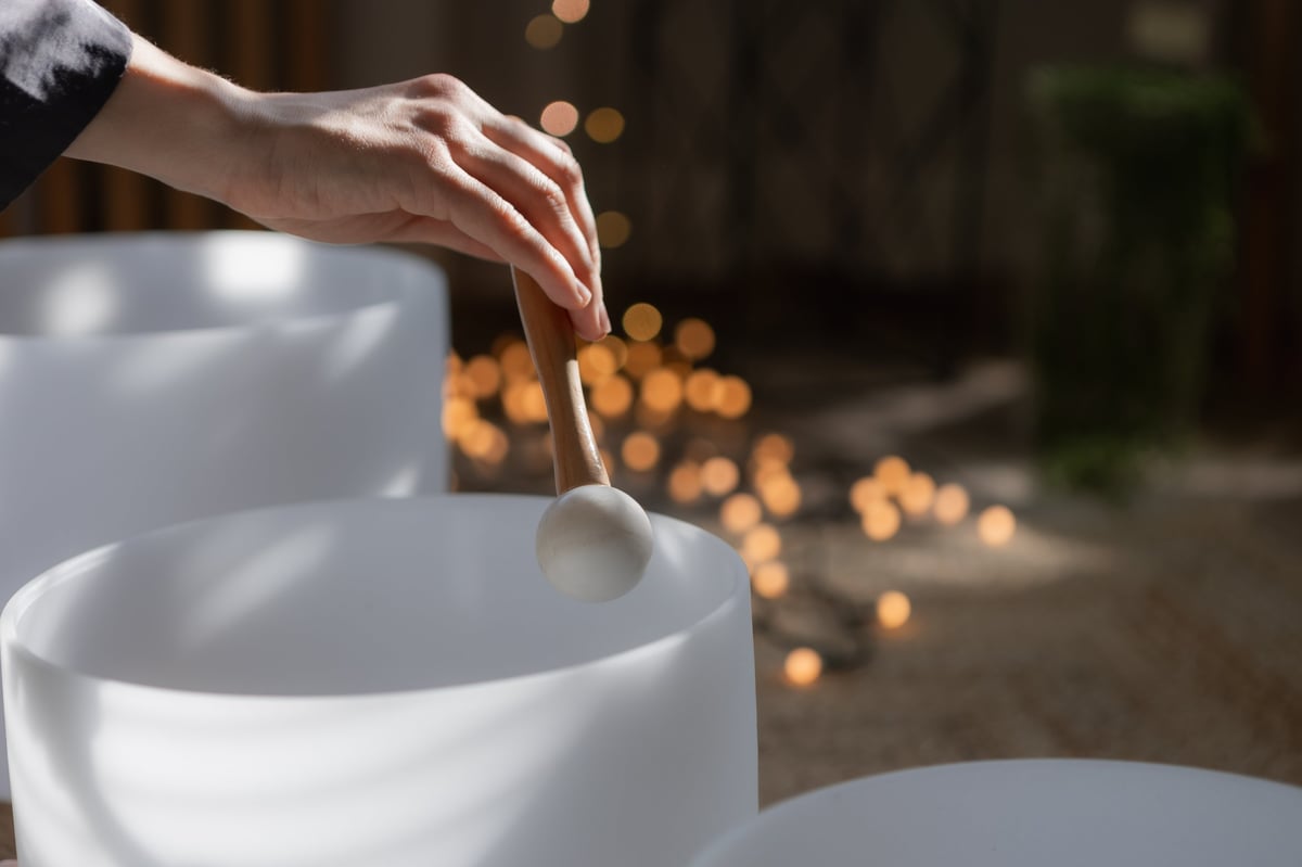 Close up of hand with mallet touching crystal singing bowl in soft natural light. Calm indoor scene for meditation, sound therapy, mindfulness, and holistic wellness concepts.